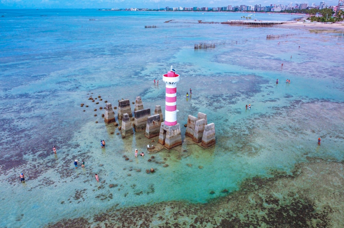 Vista aérea del Faro de Ponta Verde en Maceió, Alagoas, rodeado de piscinas naturales de agua cristalina durante la marea baja.
