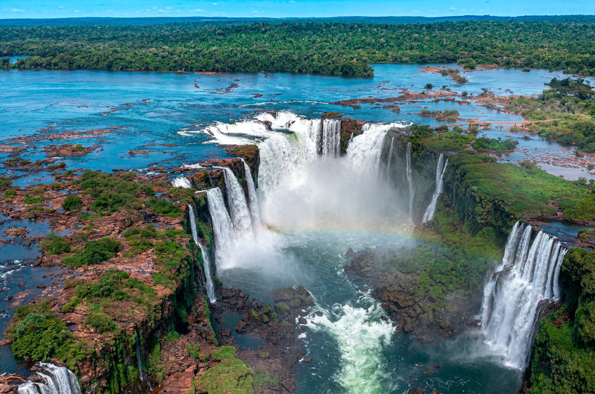 Vista aérea de la Garganta del Diablo en las Cataratas de Iguazú, mostrando el caudal de agua y la selva tropical circundante bajo un cielo despejado.