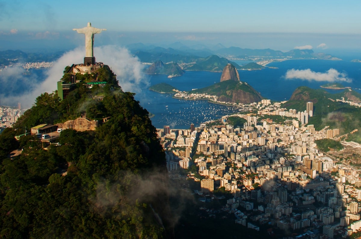 Vista aérea panorámica de la estatua del Cristo Redentor en la cima del Corcovado, con el Pan de Azúcar y la ciudad de Río de Janeiro al fondo.