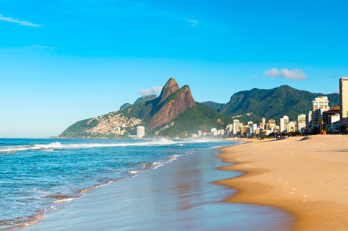 Vista panorámica de la playa de Ipanema en Río de Janeiro con el morro Dois Irmãos bajo un cielo despejado, ideal para un viaje de lujo en Brasil.