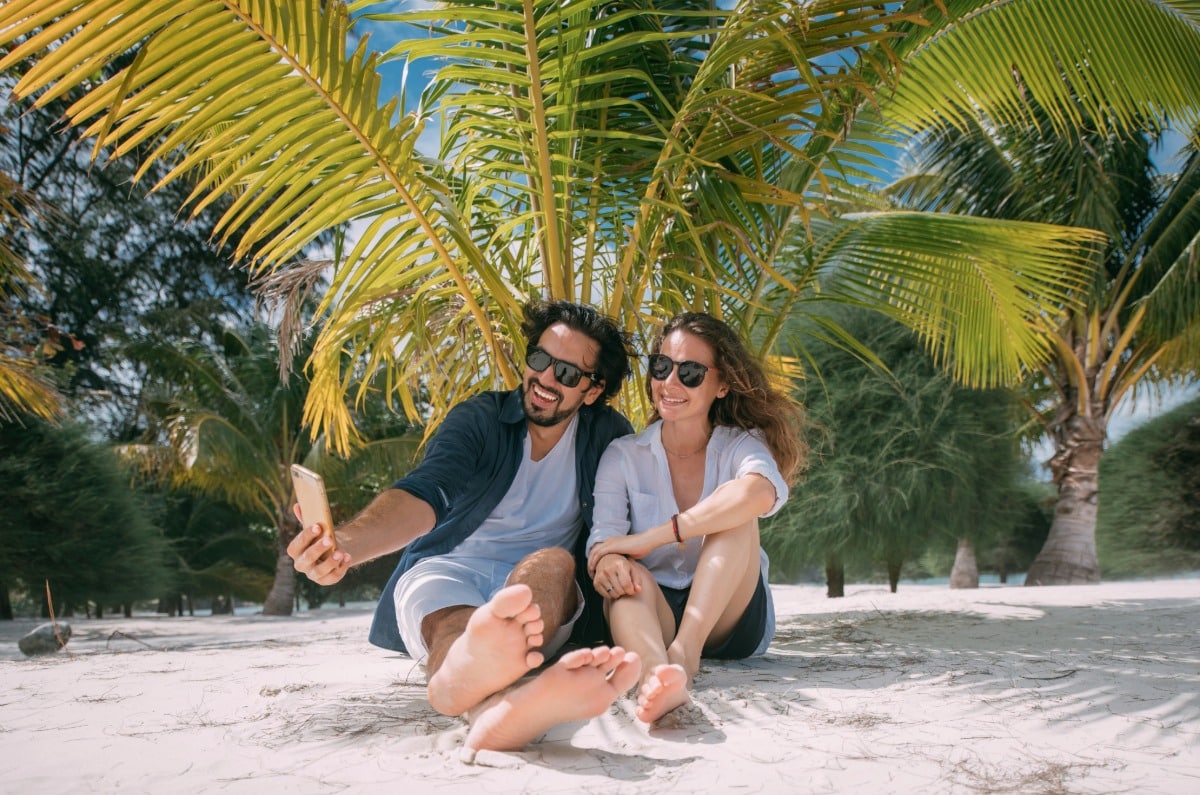Pareja de luna de miel sentada bajo las palmeras en una playa tropical de arena blanca durante su viaje exclusivo a Brasil.