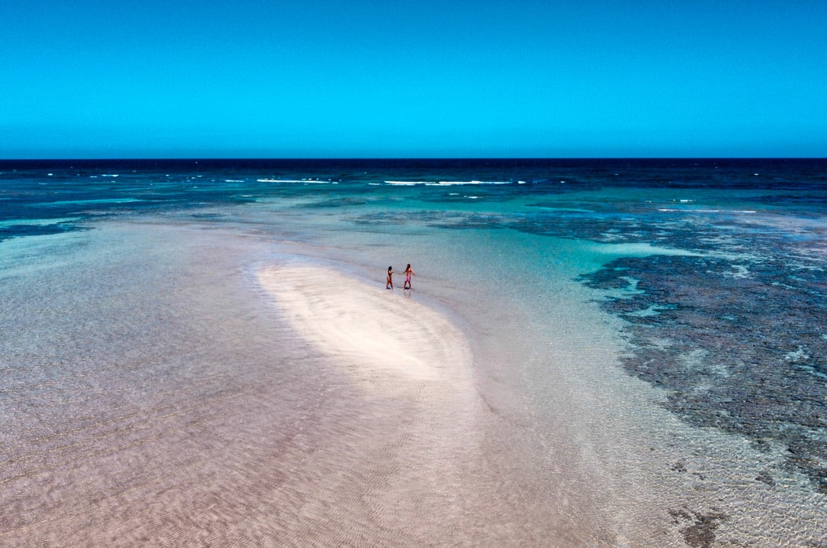 Pareja caminando por un banco de arena blanca rodeado de aguas cristalinas turquesas en Morro de São Paulo, Bahía, bajo un cielo despejado.