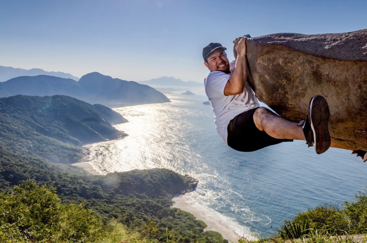 Turista posando en la famosa roca de la Pedra do Telégrafo en Río de Janeiro, capturando el efecto óptico de altura sobre las playas vírgenes de la zona oeste.