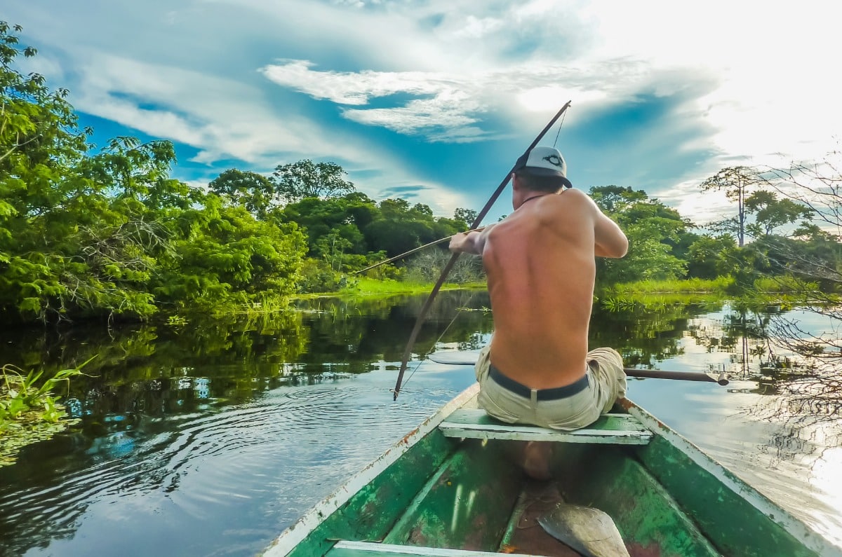 Viajero practicando pesca tradicional con arco y flecha desde una canoa en los canales del río Amazonas, Brasil.