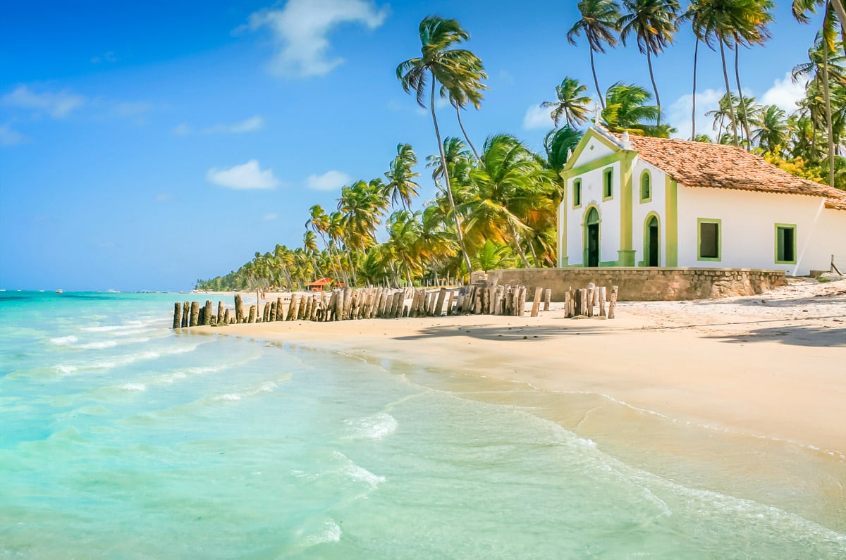 Capilla de San Benito en la orilla de la Playa de Carneiros, Pernambuco, con palmeras y aguas turquesas cristalinas en un entorno paradisíaco.