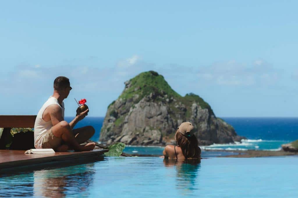 Pareja en la piscina infinita de la Pousada Maravilha con vistas a las islas y al mar durante su luna de miel en Fernando de Noronha, Brasil.