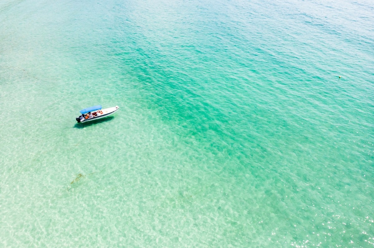 Vista aérea de una pequeña lancha navegando sobre el mar transparente de Praia do Aventureiro en Ilha Grande.