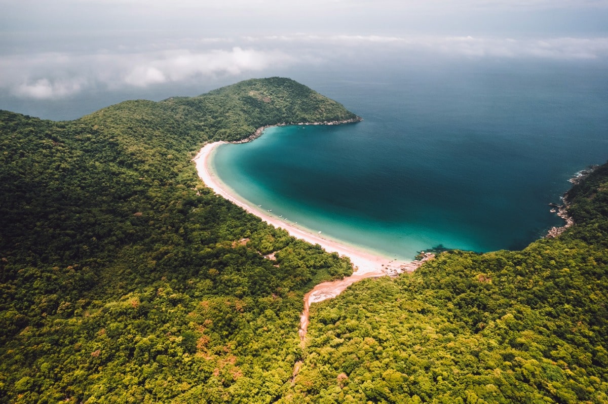 Vista aérea de una bahía semicircular de arena dorada rodeada por la densa selva atlántica en Ilha Grande, Brasil.