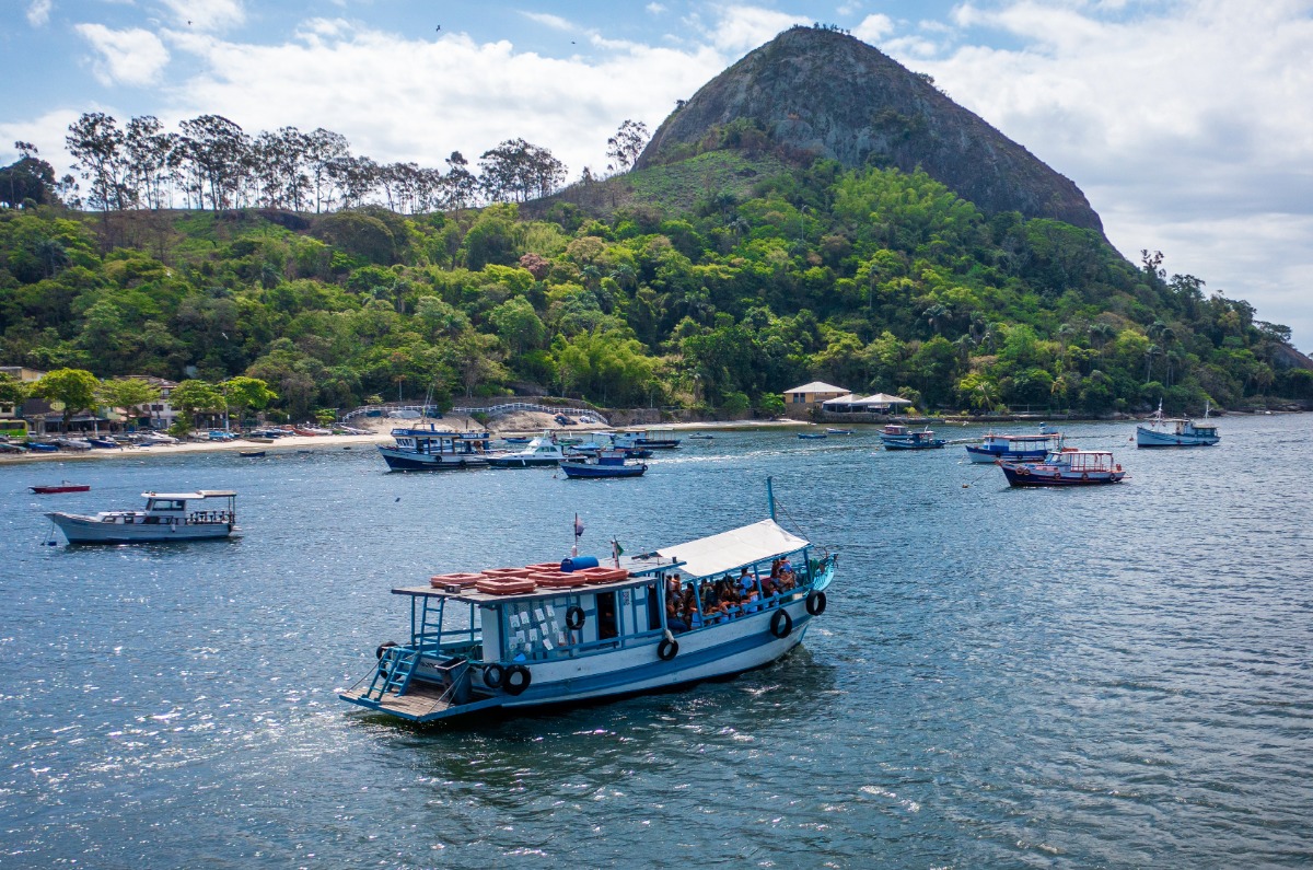 Tour en barco tradicional navegando por las aguas tranquilas de la Bahía de Guanabara en Río de Janeiro, con montañas selváticas y barcos pesqueros de fondo.