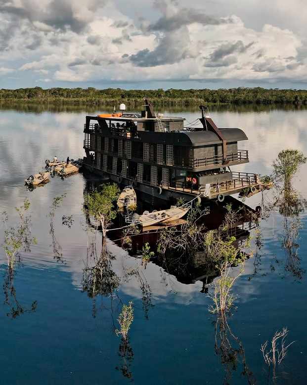 Crucero de lujo Zaltana Riverboat navegando por las aguas tranquilas del río Amazonas en Brasil, rodeado de selva y vegetación inundada.