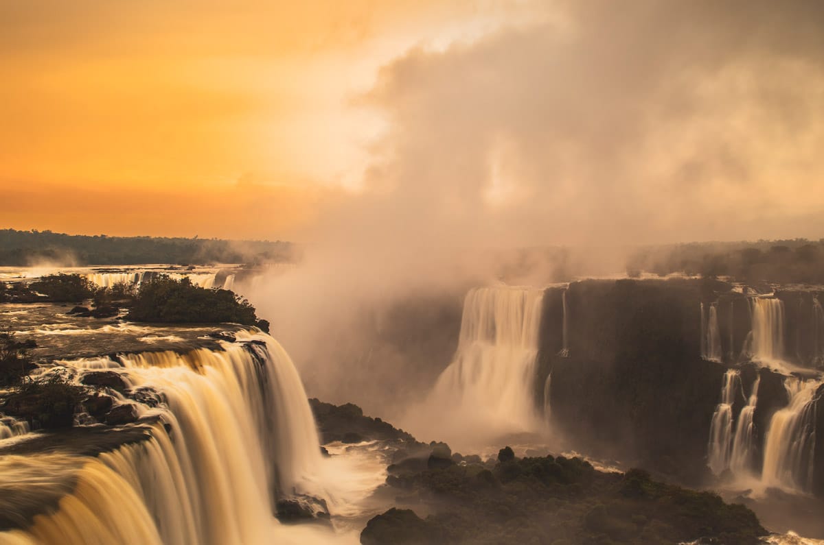 Amanecer dorado sobre las Cataratas de Iguazú con bruma matinal y los saltos de agua iluminados por la primera luz del sol.
