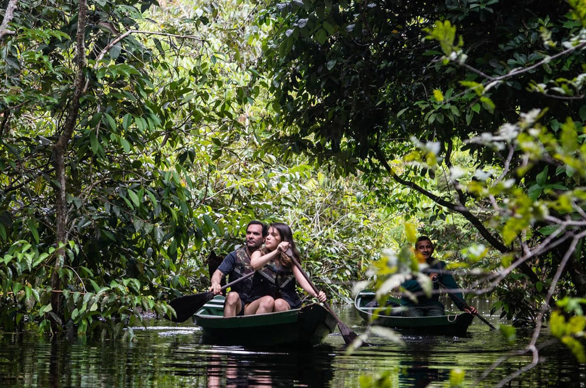 Familia navegando en canoa por un igarapé (canal) de la selva amazónica en Brasil con un guía local.