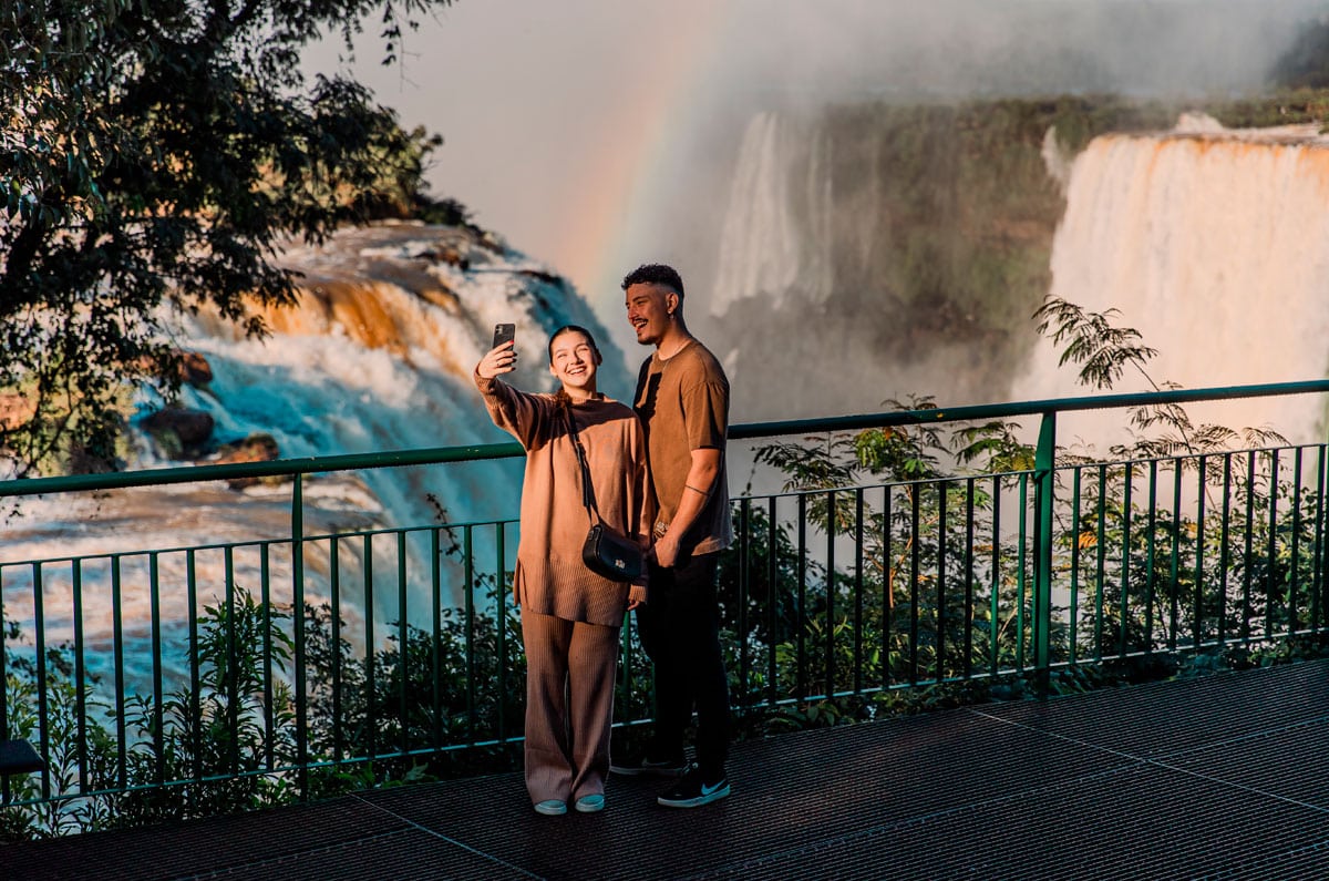 Pareja de viajeros españoles capturando un momento especial frente a las Cataratas de Iguazú con un arcoíris durante su viaje a medida.