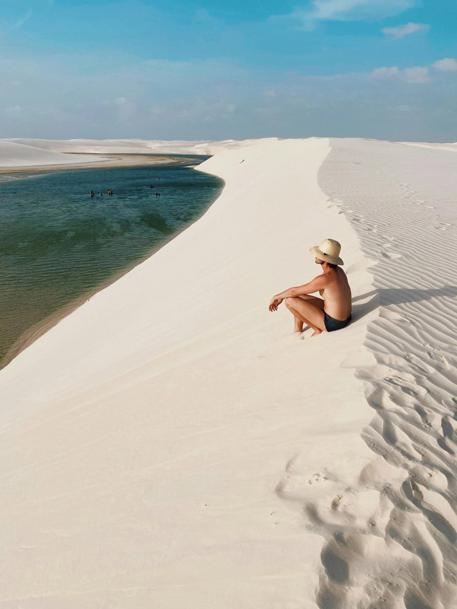 Viajero descansando en la cresta de una duna de arena blanca contemplando las lagunas de agua dulce en el Parque Nacional de los Lençóis Maranhenses, Brasil.