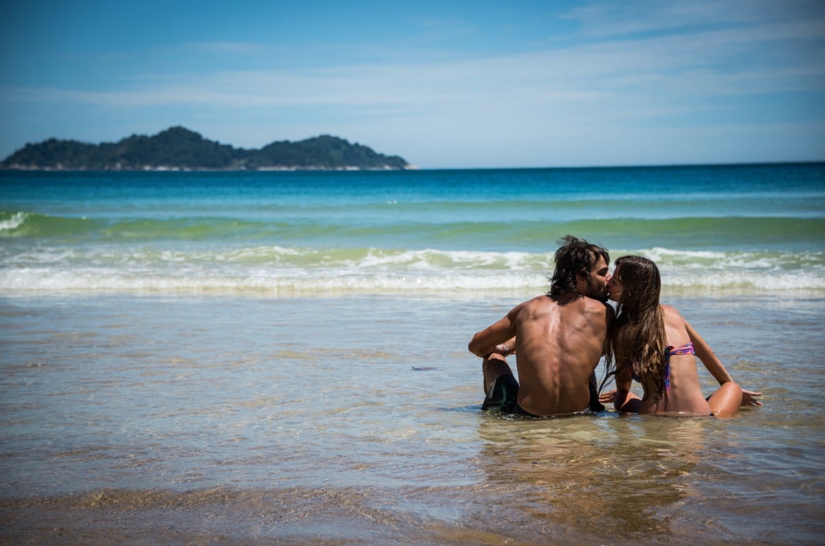 Pareja sentada en la orilla de una playa de aguas cristalinas durante su luna de miel en Ilha Grande, Brasil.