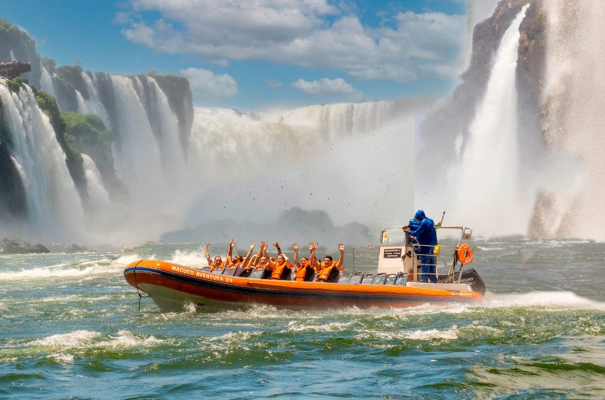 Grupo de viajeros disfrutando de la aventura del Macuco Safari en lancha rápida bajo las imponentes Cataratas de Iguazú.