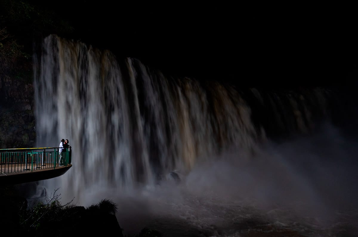 Pareja abrazada en un balcón privado frente a las Cataratas de Iguazú iluminadas durante una visita nocturna exclusiva.