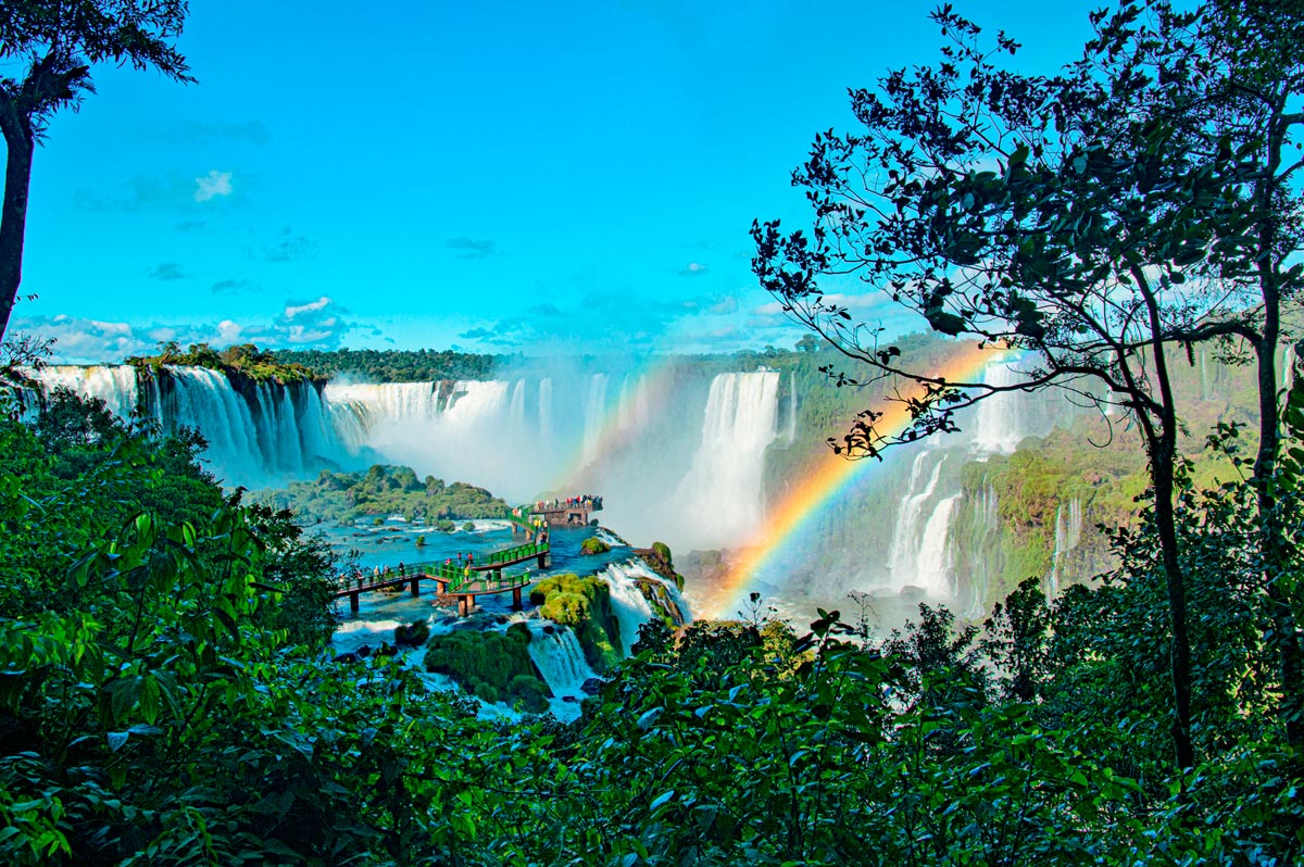 Pasarelas panorámicas sobre las Cataratas de Iguazú con un arcoíris nítido cruzando los saltos de agua y la selva tropical.