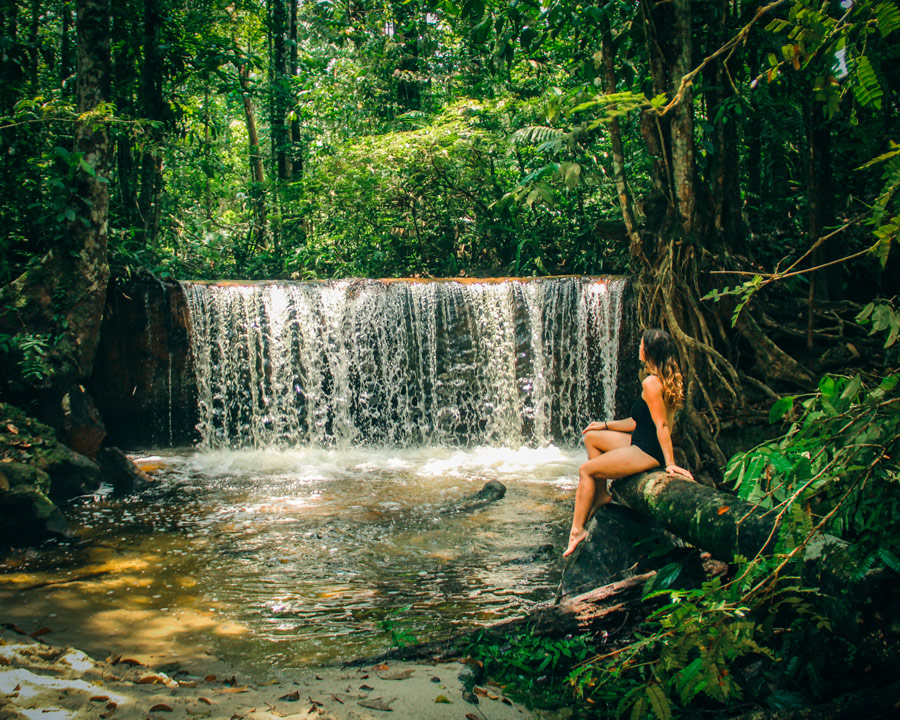 Mujer descansando frente a una cascada natural en el corazón del Amazonas, Brasil, disfrutando de un momento de paz y conexión con la selva tropical.