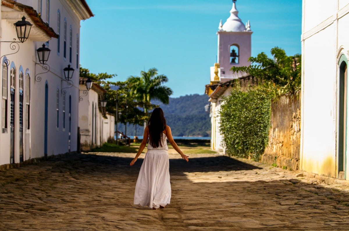 Novia paseando con vestido blanco por las calles coloniales empedradas de Paraty frente a la iglesia histórica durante su viaje por Brasil.