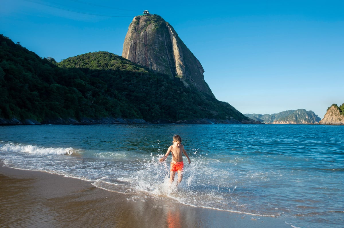 Niño jugando en la orilla de la playa de Praia Vermelha con el Pan de Azúcar de fondo en Río de Janeiro.