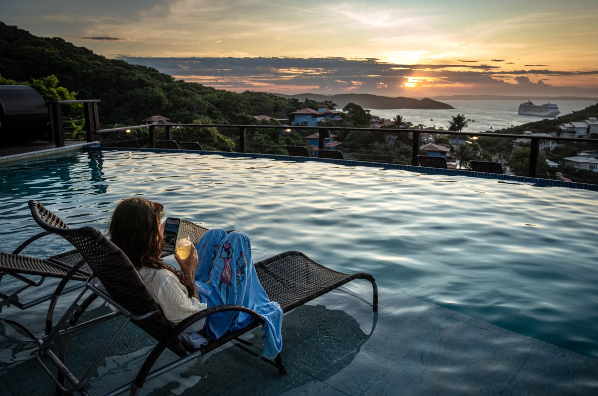 Viajera descansando en una tumbona dentro de una piscina infinita con vistas al mar y a un crucero durante el atardecer en Brasil.