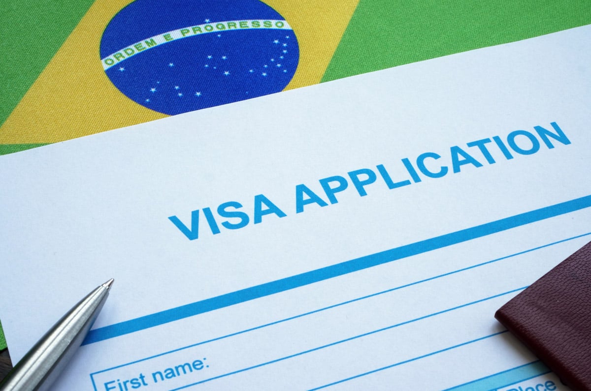 Formulario de solicitud de visado para Brasil sobre la bandera brasileña con un bolígrafo y un pasaporte.